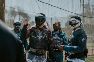 A group of paintball players wearing protective gear and masks, engaging in a strategy session outdoors.
