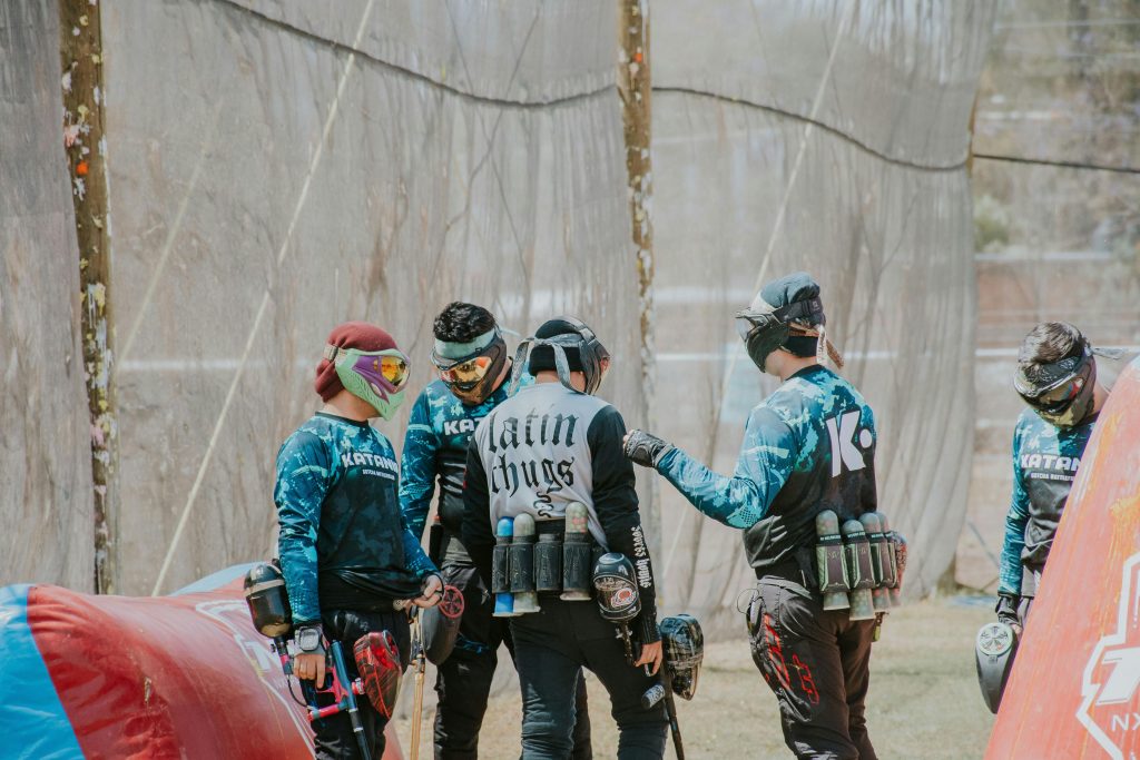 A team of paintball players in gear strategizing during a game outdoors.